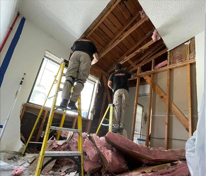 Technicians removing insulation and drywall from a storm-damaged room