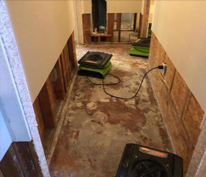 Three air movers in a room with removed flooring and drywall